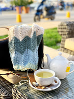 knitted shawl over a bag and teapot and a cup of tea on a table